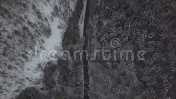 汽车和卡车在冬天的道路上行驶穿过白雪森林的鸟瞰图视频的预览图