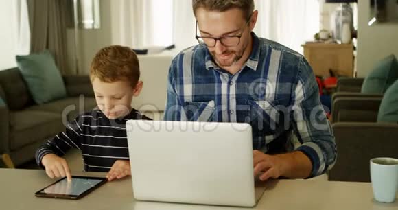 父亲和儿子使用笔记本电脑和数码平板电脑4k客厅视频的预览图