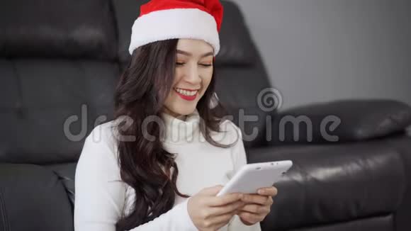 客厅里戴圣诞帽的女人用数码平板电脑视频的预览图