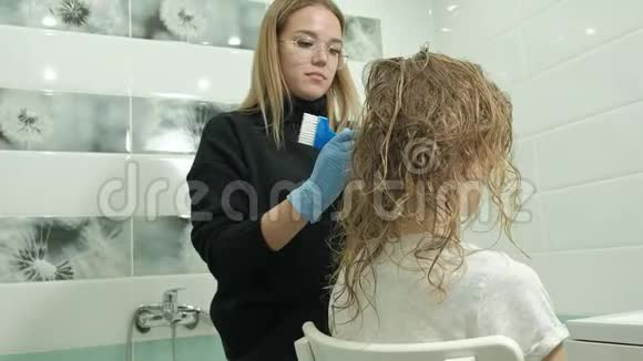 女理发师在家里的浴室里给一个年轻女人的头发涂上油漆用刷子涂上油漆视频的预览图