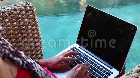 坐在巴厘岛池边的扶手椅上的一位女士正在使用她的笔记本电脑视频的预览图