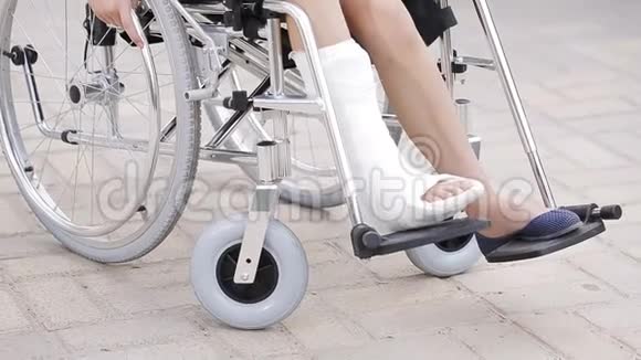 一个腿骨折的女孩坐在操场前的轮椅上视频的预览图