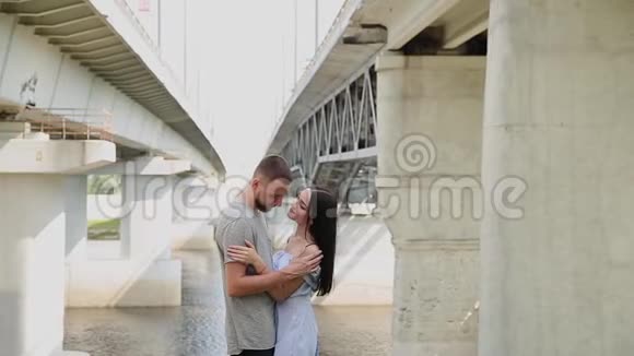 一对相爱的夫妇站在桥下拥抱和亲吻视频的预览图