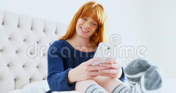 美丽的女人在床上放松时使用手机视频的预览图