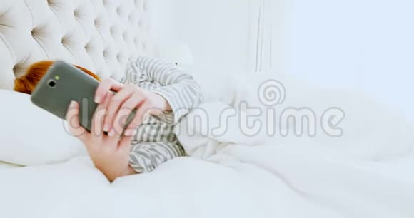 美丽的女人在床上放松时使用手机视频的预览图