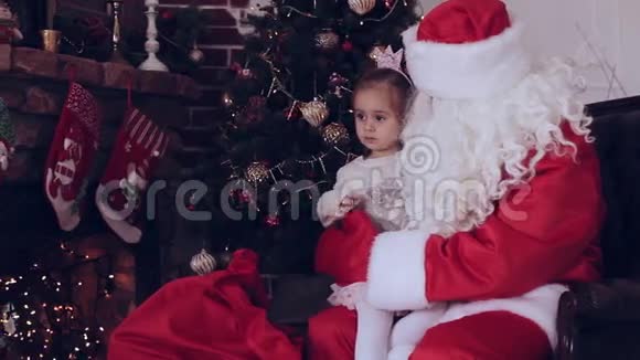 坐在圣诞老人手中的小女孩靠近圣诞树视频的预览图