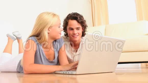 一对可爱的夫妇拿着笔记本电脑躺在地上视频的预览图