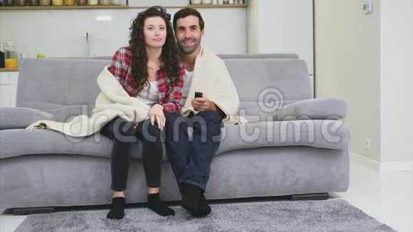 年轻夫妇在公寓里放松躺在沙发上看电影视频的预览图