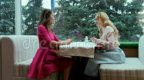 两个微笑着的年轻美女在咖啡馆的餐桌上交谈视频的预览图