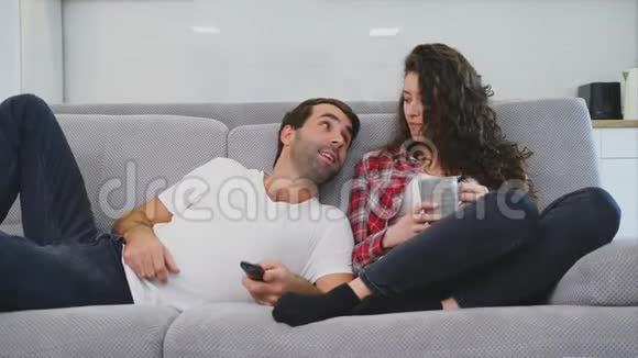 年轻夫妇在他们的公寓里放松躺在沙发上看电影视频的预览图