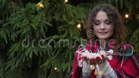 圣诞树背景下一位年轻女子手中的圣诞花环视频的预览图