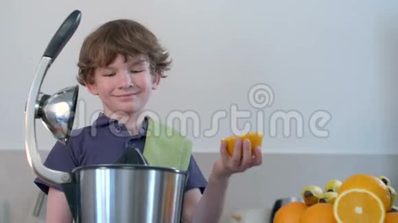 年轻有趣的白种人男孩在厨房用电榨汁机和微笑制作鲜橙果汁视频的预览图