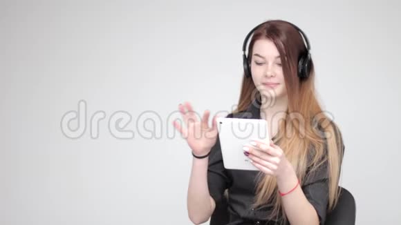 年轻漂亮的女士使用白色平板电脑听无线耳机音乐视频的预览图