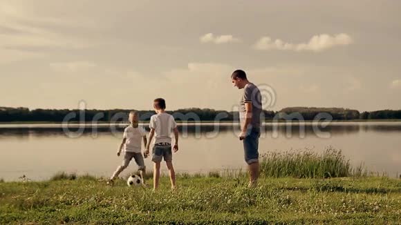 父亲和两个儿子白天在海滩上踢足球友好家庭的概念视频的预览图