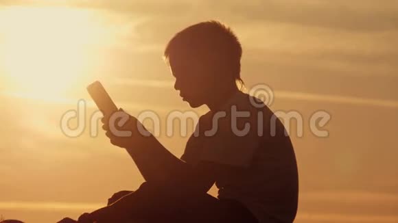 日落时分坐在山上拿着平板电脑的男孩视频的预览图