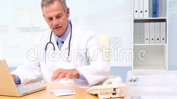 医生打电话在办公桌上用笔记本电脑视频的预览图