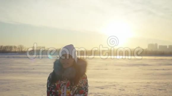快乐快乐的女人玩得开心在夕阳下的城市背景下在冬天的田野里缓慢地扔雪视频的预览图