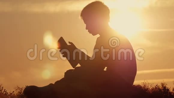 日落时分坐在山上拿着平板电脑的男孩视频的预览图