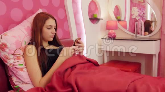 女人躺在粉红色的床上拿着电话接电话视频的预览图