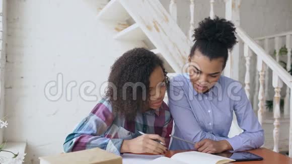 年轻的卷发混血少女坐在桌边集中精力学习功课她的长辈视频的预览图
