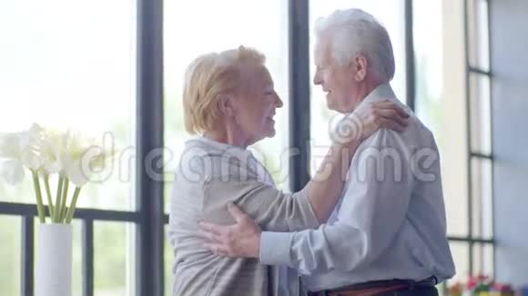 可爱快乐的老年夫妇在现代公寓他们互相交谈微笑拥抱和亲吻视频的预览图