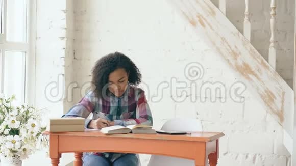年轻的卷发混血少女坐在桌边集中精力学习功课她的长辈视频的预览图