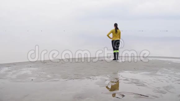 年轻苗条的女人在日落时在海边做健身瑜伽运动天与水的无缝自然背景视频的预览图