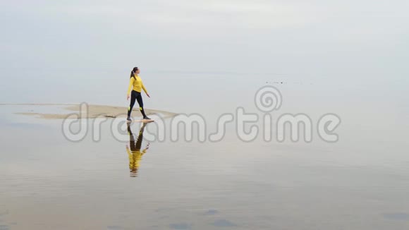 年轻苗条的女人在日落时在海边做健身瑜伽运动天与水的无缝自然背景视频的预览图