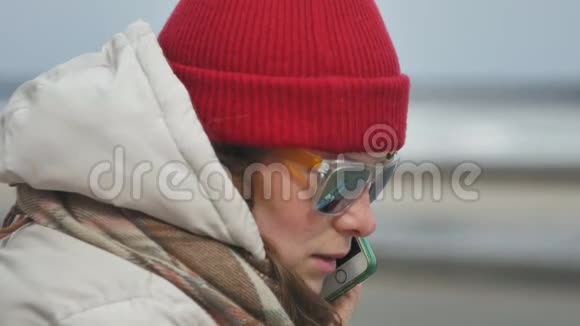 年轻漂亮的女人戴着一顶红色帽子穿着运动温暖的衣服和滚筒坐在柏油路上谈论着视频的预览图