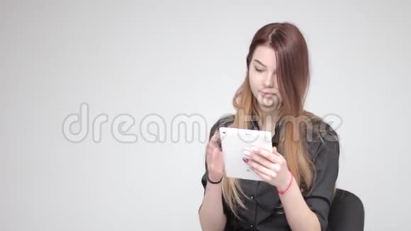 年轻貌美的女人用白色平板电脑和浅色背景的头发视频的预览图