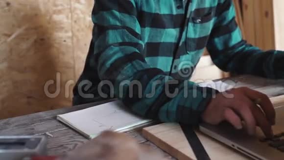 木工在他的车间里用绘图设备纸尺子铅笔和笔记本电脑工作视频的预览图
