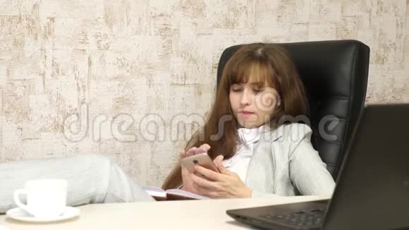 办公室里的女人在工作场所休息有电话的漂亮女商人光着脚坐在椅子上视频的预览图