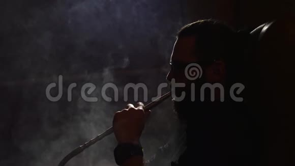 戴眼镜的小胡子男子抽着一根钩在黑色背景上慢慢地用4k的速度吹出烟雾特写视频的预览图