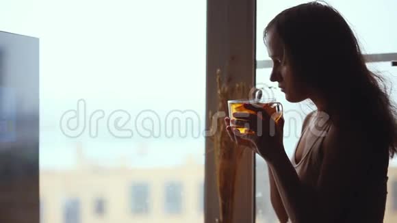 相当悲伤的女人喝茶在窗户里沉思1920x1080视频的预览图