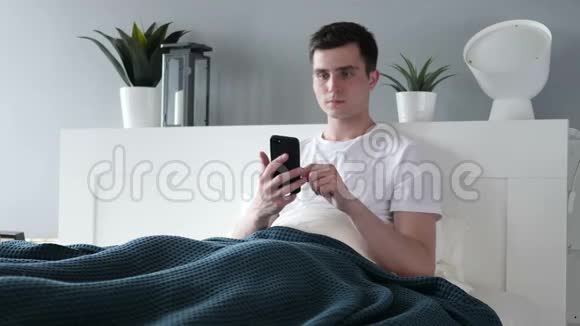 男人躺在床上用智能手机视频的预览图