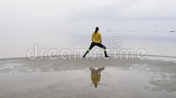 年轻苗条的女人在日落时在海边做健身瑜伽运动天与水的无缝自然背景视频的预览图