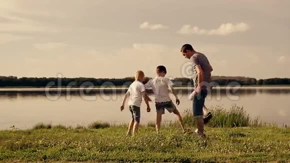 父亲和两个儿子白天在海滩上踢足球友好家庭的概念视频的预览图