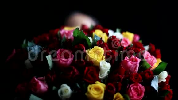 美丽浪漫的女人怀里抱着一大束花闻着一朵芬芳的五颜六色的玫瑰花在黑色上视频的预览图