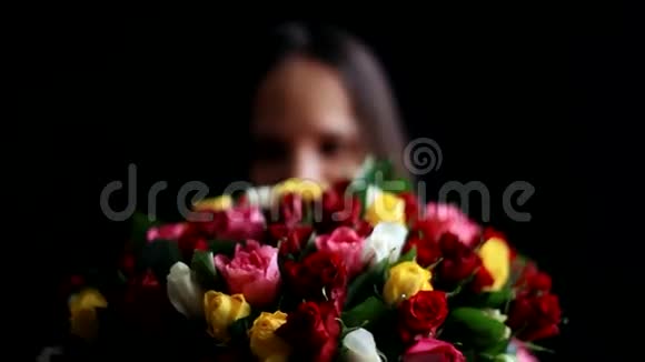 美丽浪漫的女人怀里抱着一大束花闻着一朵芬芳的五颜六色的玫瑰花在黑色上视频的预览图