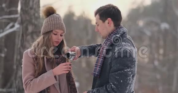 快乐的一对夫妇捧着热茶杯在冬天的风景年轻的情侣在寒假里站在一个视频的预览图