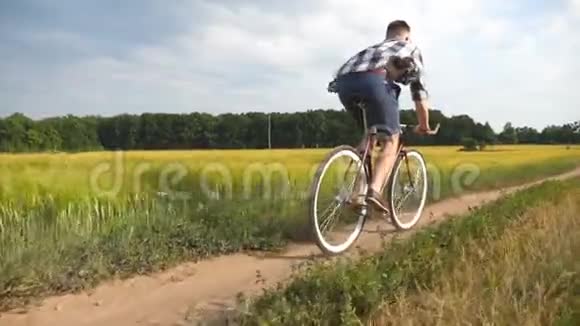 年轻人骑着老式自行车在农村公路的田野运动的家伙骑自行车沿着乡村小径户外男性视频的预览图