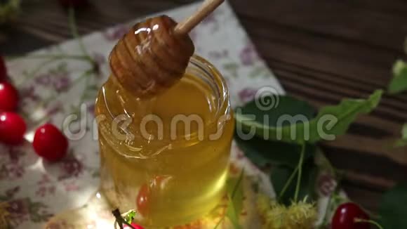 打开玻璃罐的液体蜂蜜和蜂蜜迪珀一束林登花和红樱桃在木制表面阳光的光芒视频的预览图