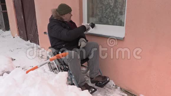 轮椅上的残疾人从雪地上清洁窗户视频的预览图