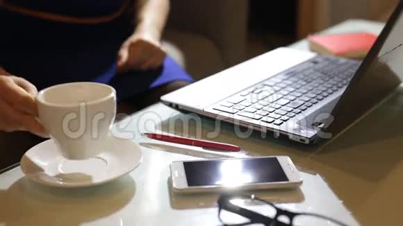 一位漂亮的年轻女士正坐在一家咖啡馆的餐厅里一边拿着咖啡杯笔记本电脑视频的预览图