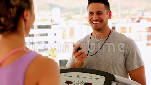 适合的女人在跑步机上跑步教练给她计时视频的预览图