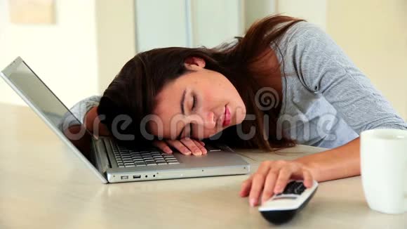 漂亮的黑发女人睡在她的笔记本电脑上视频的预览图