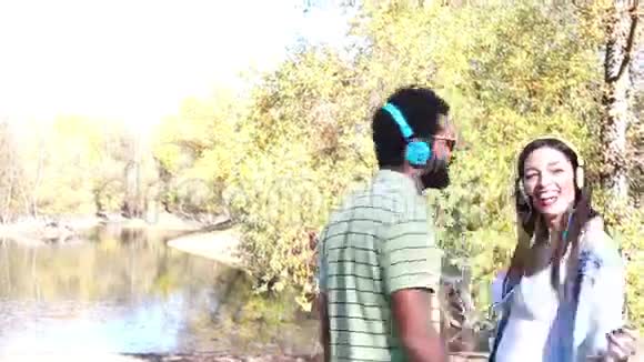可爱的夫妇带着耳机听音乐在湖边跳舞视频的预览图