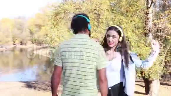 可爱的夫妇带着耳机听音乐在湖边跳舞视频的预览图