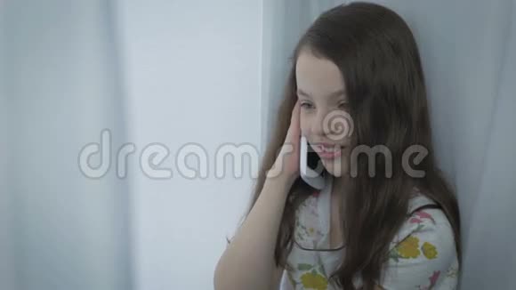 漂亮的小女孩在智能手机上情绪化地交谈和大笑视频的预览图