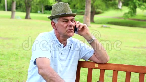 退休男子在公园长椅上打电话视频的预览图